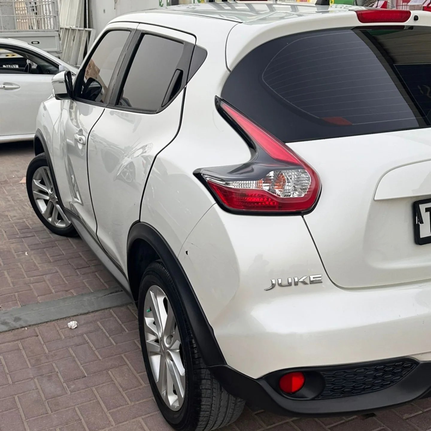 White Nissan Juke car parked on a brick pavement. The car is facing towards the left side of the image and is parked in a