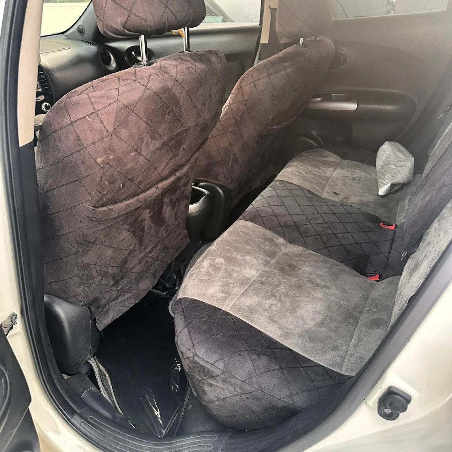 Interior of a car, specifically the front seats. The seats are covered in a gray fabric with a diamond pattern. The back