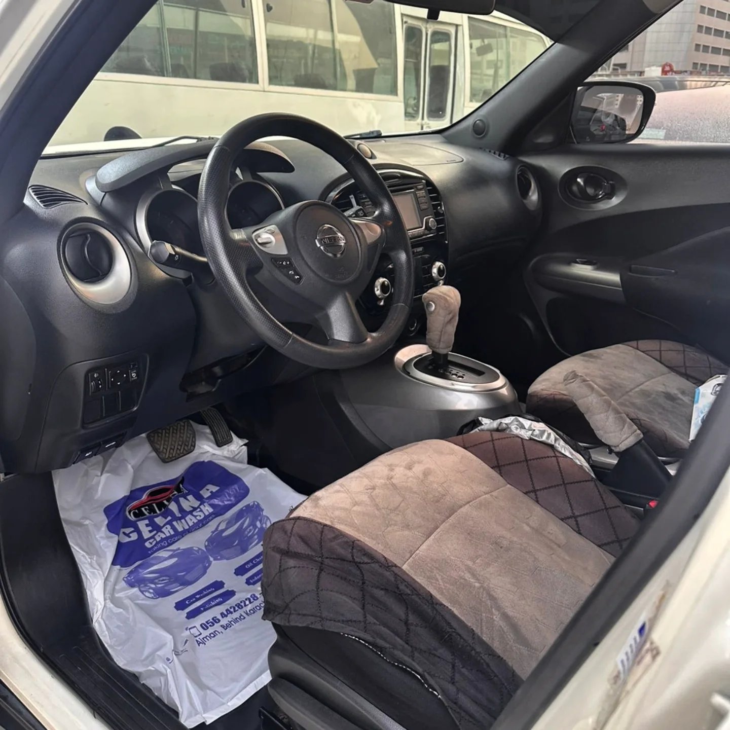 Interior of a car, specifically the driver's seat and the dashboard. The car appears to be a Nissan, as the logo of the car