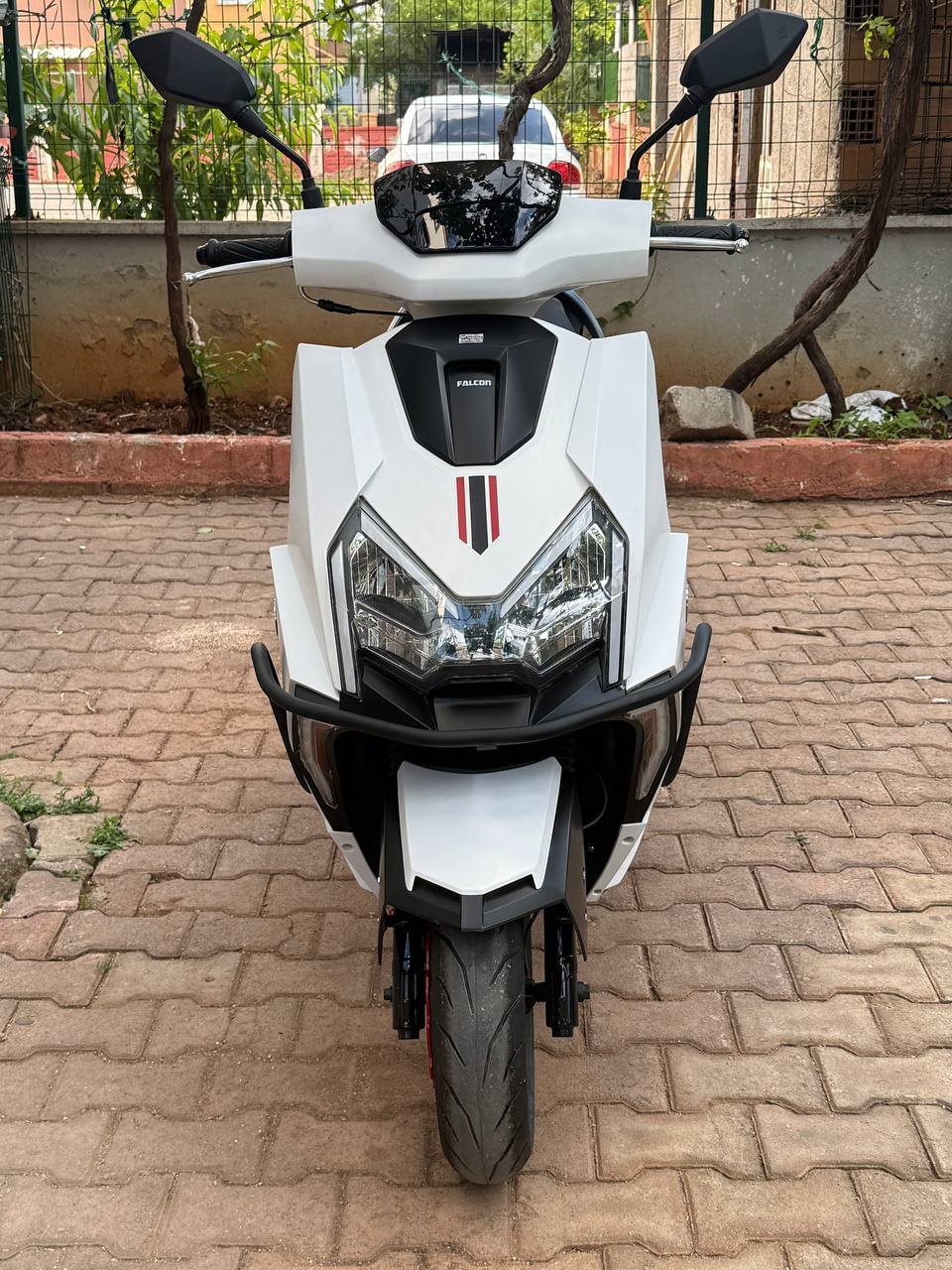 White scooter parked on a brick pavement. The scooter has a sleek and modern design with a black and red stripe on the front