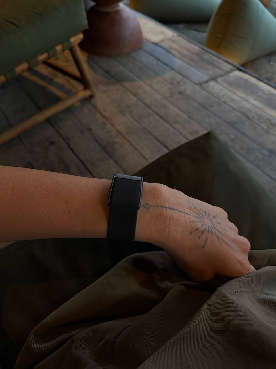 Person's arm with a black wristband on it. The person is resting their hand on a green blanket. On their wrist, there is a