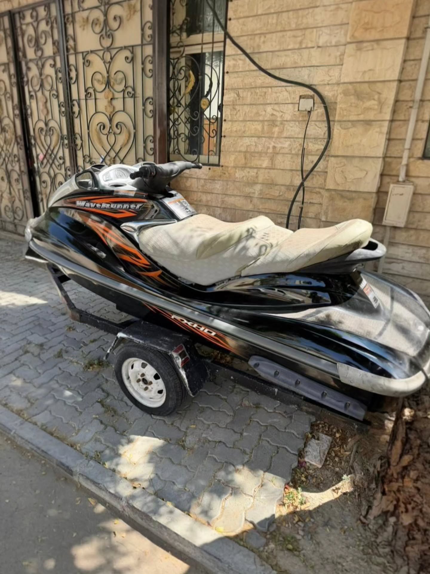Black and orange jet ski parked on a cobblestone street. The jet ski has a sleek design with a pointed nose and a pointed